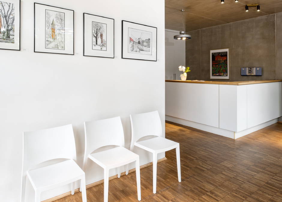 Moderne Empfangsbereich mit weißen Stühlen, Kunstwerken an der Wand und einer hellen Theke aus Holz. Ideal für Wartebereiche in Büros oder Praxen.