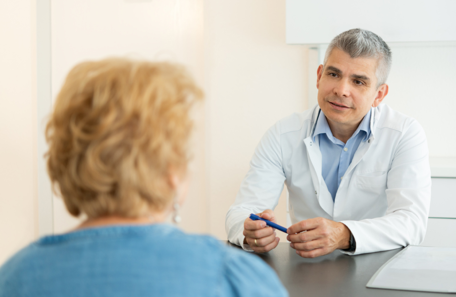Ein Arzt führt ein einfühlsames Gespräch mit einer Patientin in einer modernen Arztpraxis. Der Arzt hält einen Stift in der Hand und hört aufmerksam zu, während die Patientin ihm gegenübersitzt.