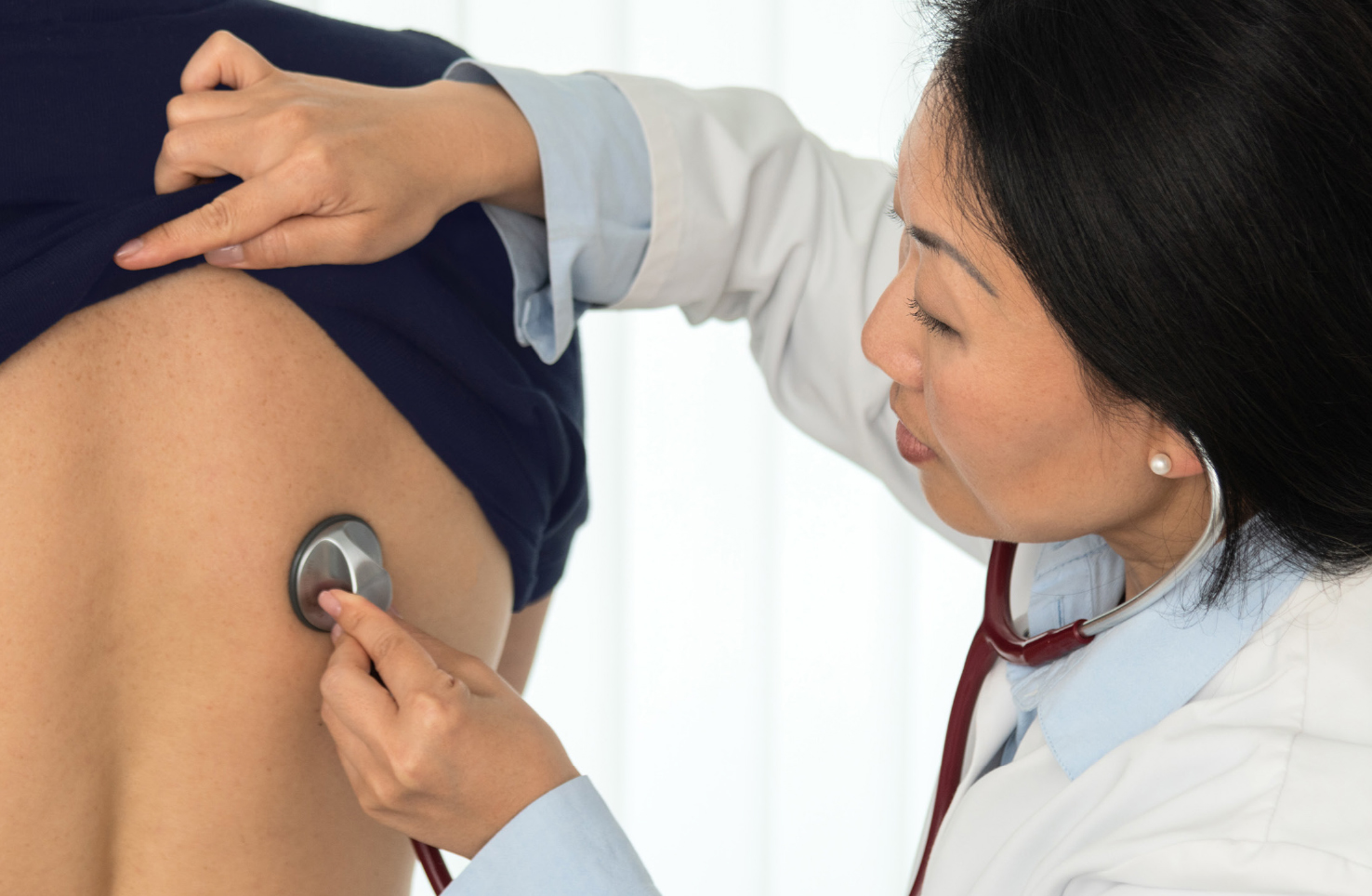 Ärztin führt eine Untersuchung mit einem Stethoskop am Rücken eines Patienten durch, um Herz- und Lungengeräusche zu überprüfen.